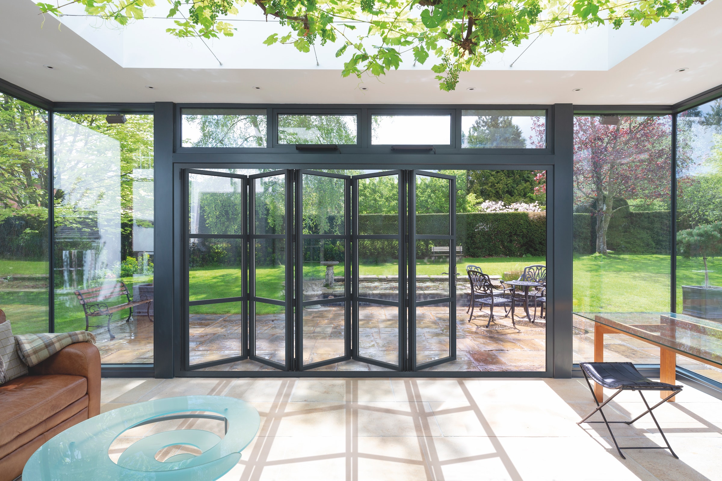 Aluco bifold doors in a conservatory, partially open with patio and garden view and sky