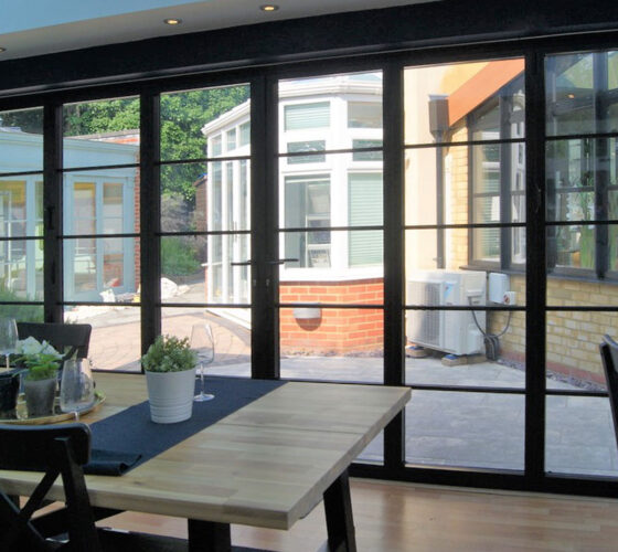 steel-look aluco bifold doors in black with a conservatory in the background